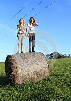 Girls standing up on package of hay