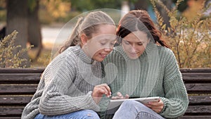 Girls students sitting in park on bench with a modern digital tablet. Teens from university, college, school, teach