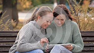 Girls students sitting in park on bench with a modern digital tablet. Teens from university, college, school, teach