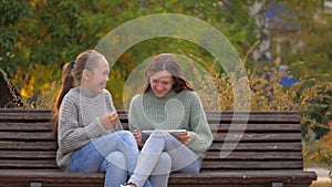 Girls students sitting in park on bench with a modern digital tablet. Teens from university, college, school, teach