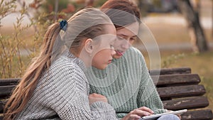 Girls students sitting in park on bench with a modern digital tablet. Teens from university, college, school, teach