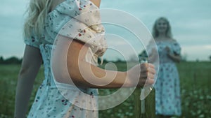 Girls in summer dresses in the field - a blonde opens a bottle of wine and goes to her friend