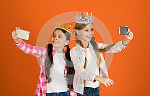 Girls taking selfie photo smartphone camera. Spoiled children concept. Egocentric princess. Kids wear golden crowns