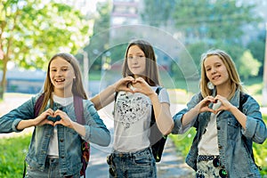 Girls teenagers in summer in the park in fresh air. Gesture hands show the heart of love. Dressed in casual clothes. The