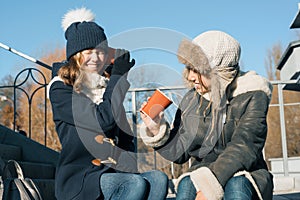 Girls teens shout into a megaphone paper cup, dressed in winter clothes, sunny winter day