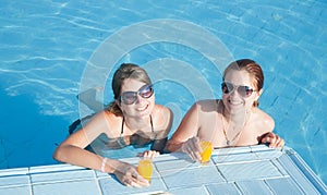 Girls in tropical pool with orange juice