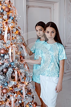 Girls twins in front of the fir-tree. New year`s eve. Christmas. Cozy holiday at the fir-tree with lights
