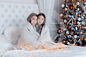 Girls twins in front of the fir-tree. New year`s eve. Christmas. Cozy holiday at the fir-tree with lights