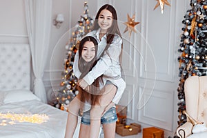 Girls twins in front of the fir-tree. New year`s eve. Christmas. Cozy holiday at the fir-tree with lights