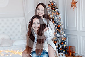 Girls twins in front of the fir-tree. New year`s eve. Christmas. Cozy holiday at the fir-tree with lights