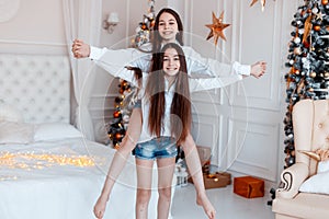 Girls twins in front of the fir-tree. New year`s eve. Christmas. Cozy holiday at the fir-tree with lights