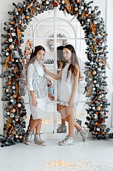 Girls twins in front of thearch mirror. New year`s eve. Christmas. Cozy holiday at the fir-tree with lights