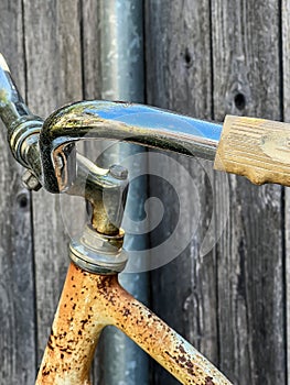 Girls well made vintage, but rust covered bike handlebars and frame resting against a wood fence