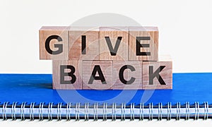 GIVE BACK - a word made of wooden blocks with black letters, a row of blocks is located on a blue Notepad