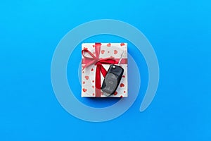 Give gift car key concept top view. Present box with red ribbon bow, heart and car key on blue colored background