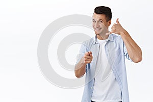 Give me a call. Portrait of handsome cheerful caucasian guy showing phone sign and pointing camera, want to have