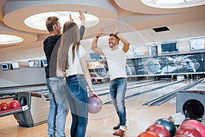 Give me high five. Young cheerful friends have fun in bowling club at their weekends