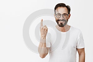 Give me one minute to dress up. Charming carefree friendly-looking bearded man in trendy glasses, showing index finger photo