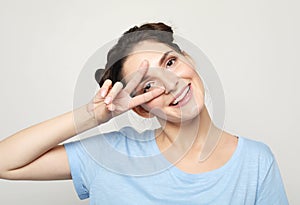 Give peace a chance. Portrait of a pretty brunette woman showing the peace sign on grey background.