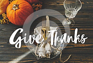 Give Thanks text handwritten on thanksgiving dinner table setting. Plate, linen, pumpkin with autumn flowers on rustic table.