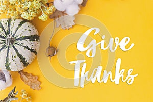 Give thanks text on pumpkin, autumn flowers, leaves on yellow background flat lay. Happy thanksgiving Seasonal greeting card,