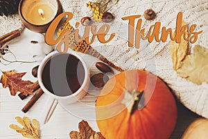 Give Thanks text sign on warm tea, pumpkins and spices at cozy sweaters, autumn leaves, candle. Seasons greetings. Happy