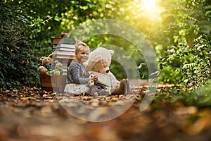 Give them a happy childhood. a little girl reading to her toys while out in the woods.