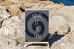 Give it a try symbol. Concept word Give it a try on beautiful black chalk blackboard. Beautiful red stone blue sea background.
