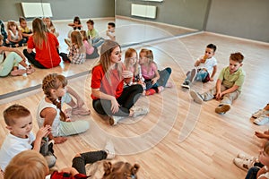 Giving advice. A group of little dancers sitting on the floor gathered around their female dance teacher. Full length