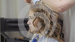 Giving the blonde hair shape and volume. Styling curls on the head of a young girl.