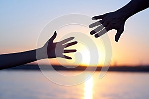 Giving a helping hand. Silhouette Two hands, man and woman, reaching towards each other at sky sunset