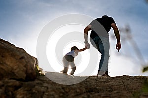 Young father giving helping hand to his son walking over mountain top as a metaphor of fatherhood photo