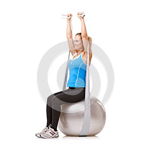 Giving her arms a great workout. A young blonde woman sitting on an exercise ball while pulling a resistance band