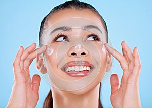 Giving her skin a little TLC. Studio shot of an attractive young woman applying moisturizer against a blue background.