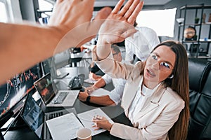 Giving high five. Team of stockbrokers works in modern office with many display screens