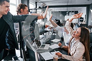 Giving high five. Team of stockbrokers works in modern office with many display screens