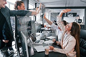 Giving high five. Team of stockbrokers works in modern office with many display screens