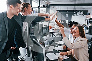 Giving high five. Team of stockbrokers works in modern office with many display screens