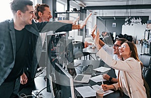 Giving high five. Team of stockbrokers works in modern office with many display screens