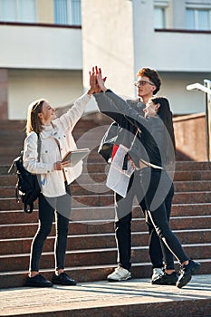 Giving high five to each other. Three young students are outside the university outdoors