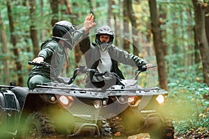 Giving high fives by the hands. Two male atv riders is in the forest together