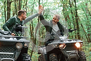 Giving high fives by the hands. Two male atv riders is in the forest together