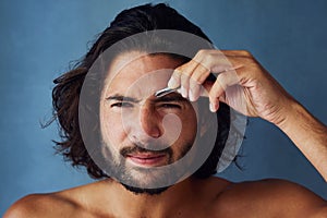 Giving his brows some defined shape. Studio portrait of a handsome young man plucking his eyebrows against a blue