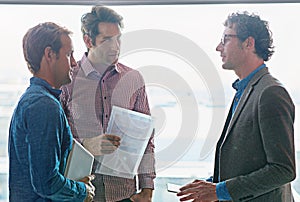 Giving his team a few words of advice. male coworkers talking while standing in front of a window in an office.