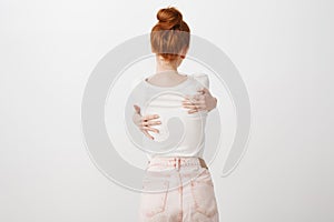 Giving myself warm hug to forget troubles. Portrait of thin young european redhead with bun hairstyle, hugging herself