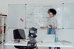 Giving online class. Young afro american female English teacher standing near whiteboard and smiling, explaining rules
