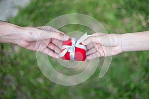 Giving red gift box in with hands On special days for special person, on grass background. Wedding ring box