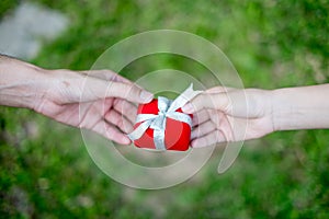 Giving red gift box in with hands On special days for special person, on grass background. Wedding ring box