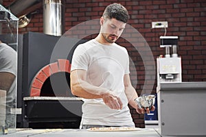 Giving some solt. Baker in white shirt throws spices to make delicious pizza for an order in restaurant