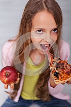 Giving in to temptation - young girl choosing the slice of pizza instead of the apple